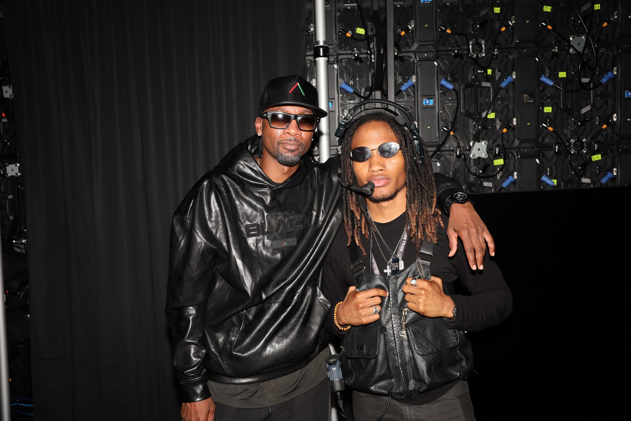 Two men in black leather jackets embrace backstage at the Actively Black show